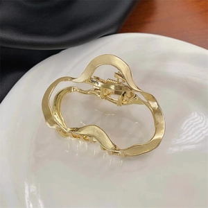 Macro shot of wavy geometric gold metal hair claw clip on white ceramic plate