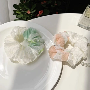 Detail of green and pink floral organza hair scrunchies with pleated texture on a white plate