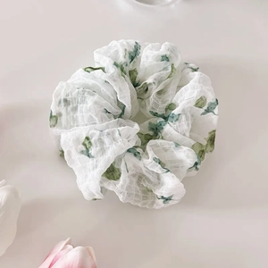 Détail du chouchou blanc à motifs floraux verts avec une texture de tissu en maille