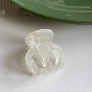 Macro shot of small pearlescent white hair claw clip with iridescent finish and curved teeth