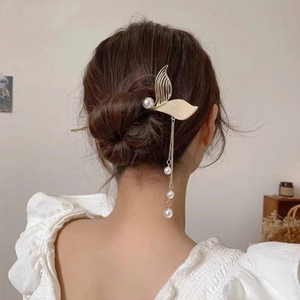 Detail of mermaid tail hair pin with hanging pearls and tassels on golden finish