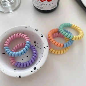 Gros plan d'élastiques à cheveux spirales pastel dans un bol blanc décoratif