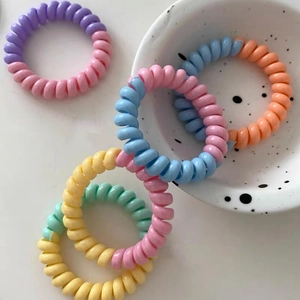 Élastiques à cheveux spirales bicolores aux tons pastels posés sur un plateau blanc