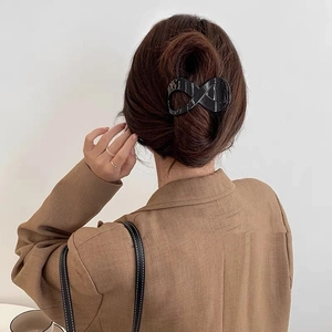 Detail of a glossy black infinity-shaped claw clip for a minimalist back hairstyle