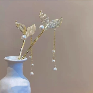Detailed close-up of golden mermaid tail hairpins with pearl tassels and rhinestones