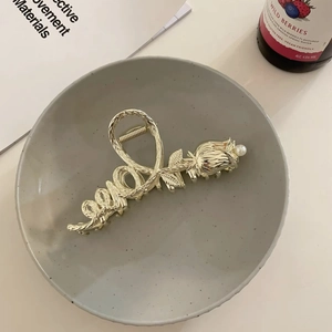 Detailed view of a golden rose hair claw clip with a white pearl on a ceramic tray