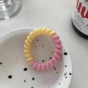 Détail macro de l'élastique spirale bicolore jaune et rose dans un bol en céramique