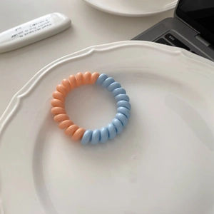 Vue détaillée de l'élastique à cheveux spirale bicolore en bleu pastel et orange doux