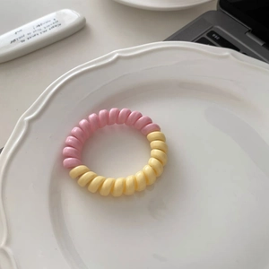 Détail d'un élastique spirale bicolore rose et jaune posé sur une assiette en porcelaine