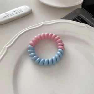 Gros plan d'élastiques à cheveux spirale rose et bleu sur un plateau en céramique blanc
