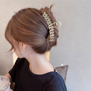 Dettaglio di un grande fermaglio per capelli dorato traforato con scritte su uno chignon