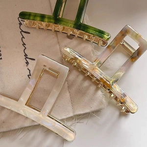 Close-up of three acetate hair claws in green, white, and tortoiseshell on linen fabric