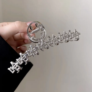 Dettaglio della grande molletta per capelli argento con caratteri Haha e design smiley
