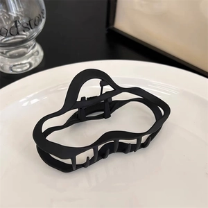 Détail d'une grande pince à cheveux noire mate avec des lignes ondulées sur un plat blanc