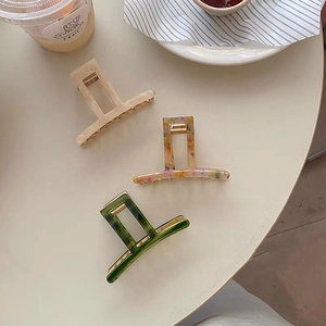 Three acetate hair claws with marble patterns and hollow rectangular design on a table