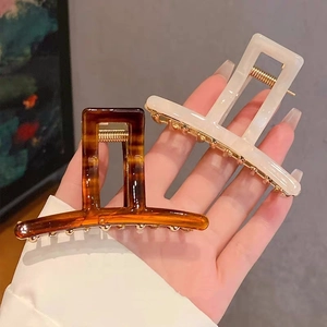 Detail view of square acetate hair claw clips in amber and pearl white held by hand