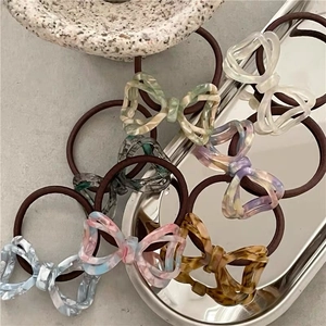 Detail of assorted acetate bow hair ties in multiple colors on a textured stone tray