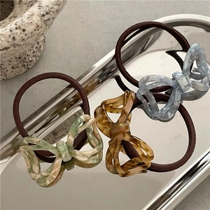 Three acetate bow ponytail holders in green, amber, and blue on a silver tray