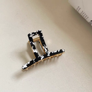 Detail of a rectangular hollow hair claw clip with black and white marble pattern and gold spring