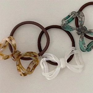 Close-up of three acetate bow hair ties in amber, white, and marble green textures