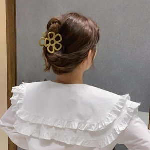 Dettaglio del fermaglio a fiore oro opaco indossato su uno chignon di capelli castani