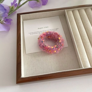 Detailed macro view of a pink tweed knit hair tie with colorful specks in a jewelry box