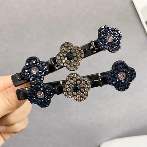 Détail de deux barrettes noires à fleurs ornées de strass bleus et couleur champagne