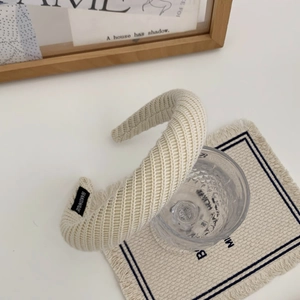 Détail d'un serre-tête tricoté blanc crème montrant l'étiquette faite main et la texture