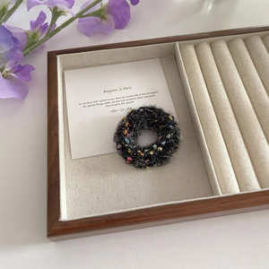 Close-up of knit tweed scrunchie with colorful dots in a wooden jewelry display tray
