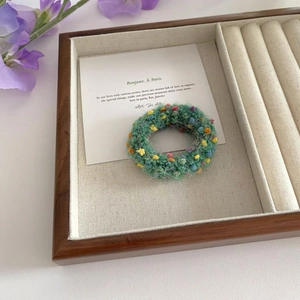 Close-up of a green hand-knitted hair scrunchie with colorful floral knots in a wooden box