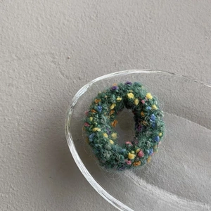 Close-up of forest green knitted mohair hair tie with colorful texture in glass dish