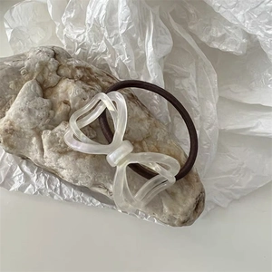 Close-up of a pearlescent white acetate bow hair tie on a minimalist stone background