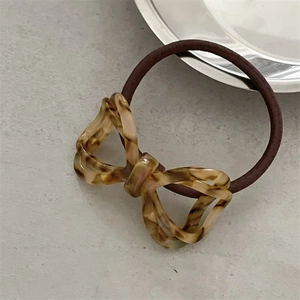 Macro shot of amber acetate bow hair tie with hollow design on minimalist grey surface