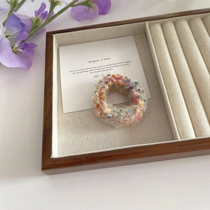 Close-up of colorful fuzzy knit hair scrunchie on a wooden tray with purple flowers