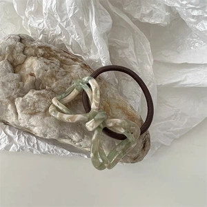 Detailed shot of a green acetate bow hair tie on a white paper and stone background