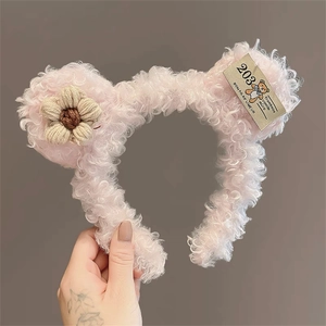 Detailed close-up of a pink plush bear ear headband with a knit flower and brand label