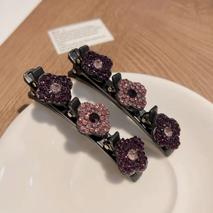 Vue détaillée de deux barrettes à fleurs avec cristaux violets et roses sur clips métalliques