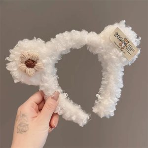 Detail of white plush bear headband featuring a knit flower and designer tag decoration