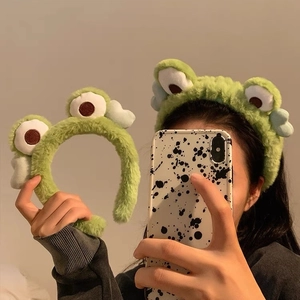 Detailed close-up of the green plush frog headband with embroidered big eyes and blue wings