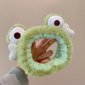 Detail of plush green frog headband with cute white eyes and bow for makeup and skincare
