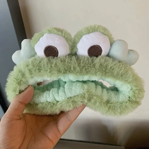 Close-up of soft green plush frog headband with large cute eyes and elastic texture
