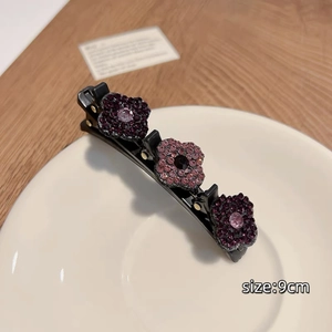 Détail d'une barrette tressée de 9cm avec cristaux violets et roses sur une assiette blanche