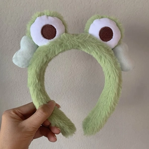 Detailed view of plush green frog headband with soft fur and embroidered big eyes