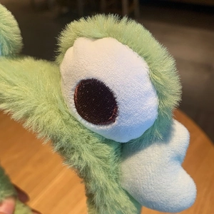 Close-up of soft plush frog headband showing light green faux fur and embroidered eyes