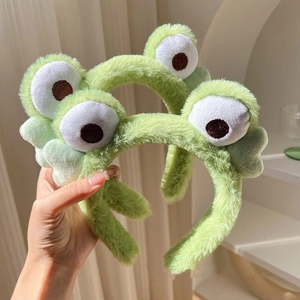 Close-up of soft green plush frog headband with cute big cartoon eyes and fuzzy texture