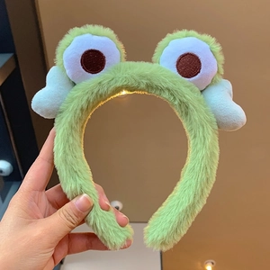 Detail of plush green frog headband featuring glowing LED eyes and soft fuzzy texture