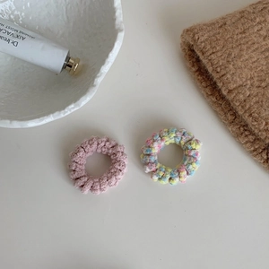 Gros plan d'élastiques à cheveux tricotés en spirale rose et macaron sur une table élégante