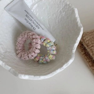 Gros plan d'élastiques à cheveux en peluche rose et motifs colorés dans un bol blanc