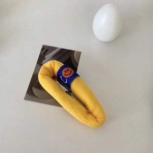 Detail of yellow knit sponge hair clip featuring blue woven label with smiley face icon