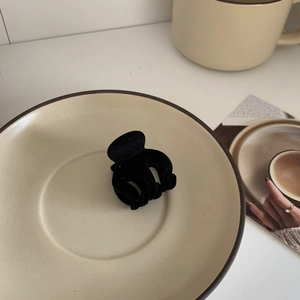 Detailed view of a black flocked velvet hair claw clip on a minimalist ceramic tray